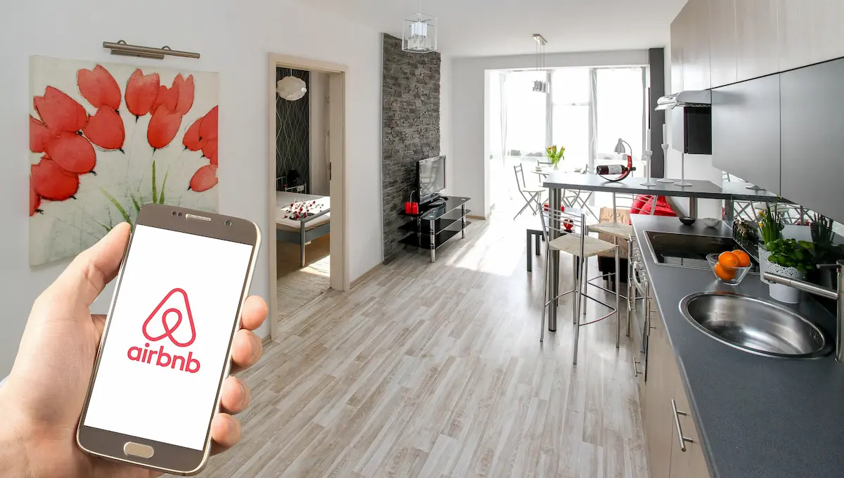 Guest holding a phone with the Airbnb app open inside a bright, freshly cleaned short-stay apartment